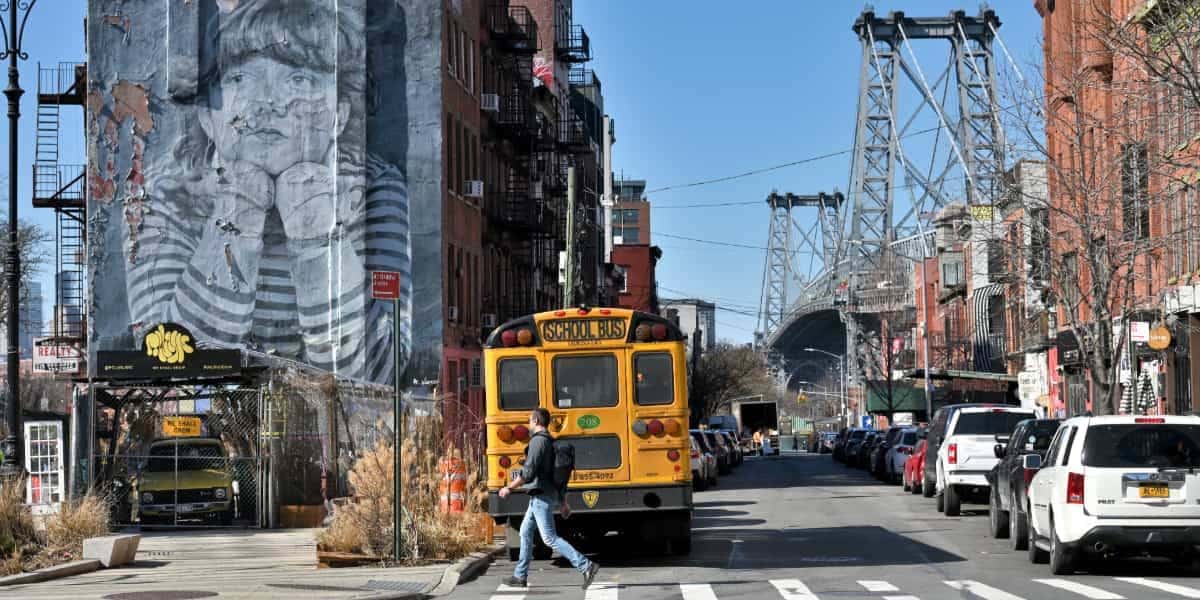 Street view in Brooklyn near Williamsburg Bridge with school bus, mural, and city life—representing trusted brooklyn family lawyer services.