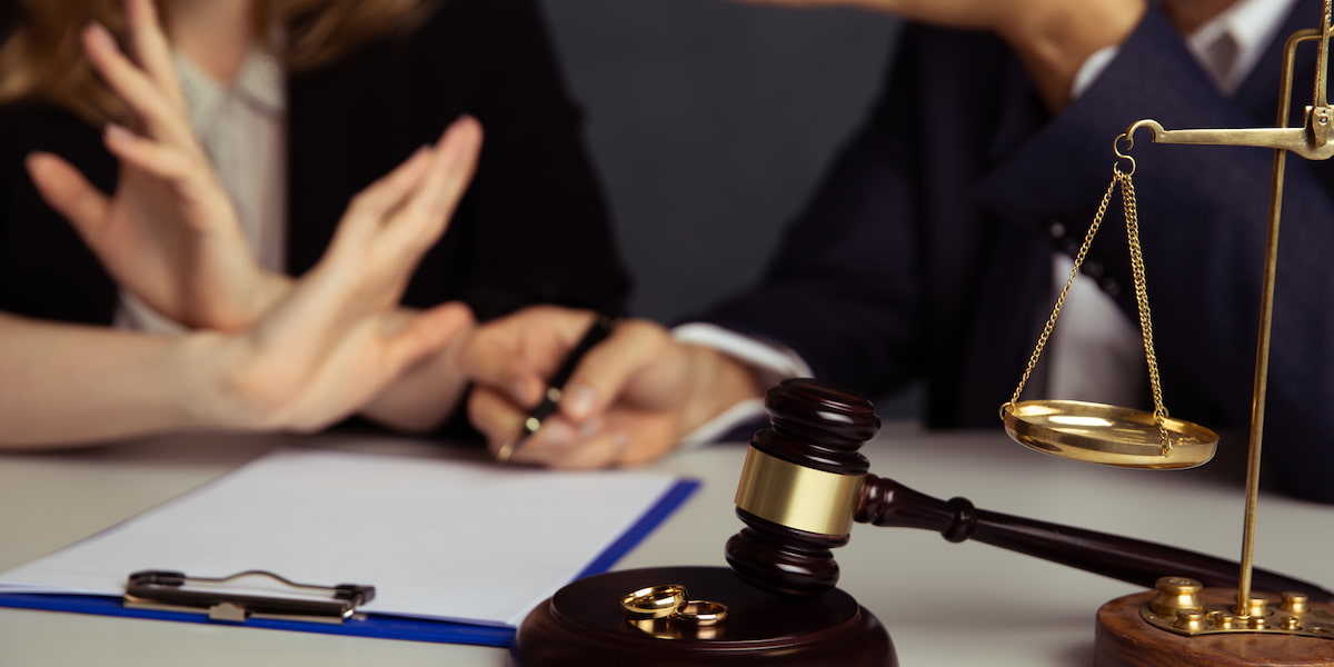Couple discussing separation agreement with scales of justice and wedding rings on table